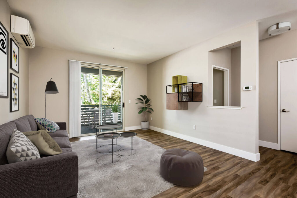 Living room with large glass sliding door out to balcony patio, with mounted air conditioning unit on the wall and several decorative items