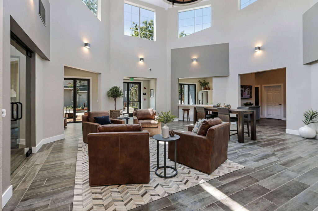 Leasing center with four armchairs and a view of the kitchen area featuring bar-height seating, with large windows providing natural light throughout the space