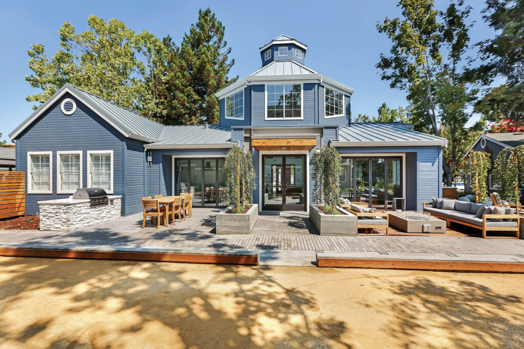 Exterior view of blue leasing center building with outdoor seating, grilling, fire pits and Bocce Ball court