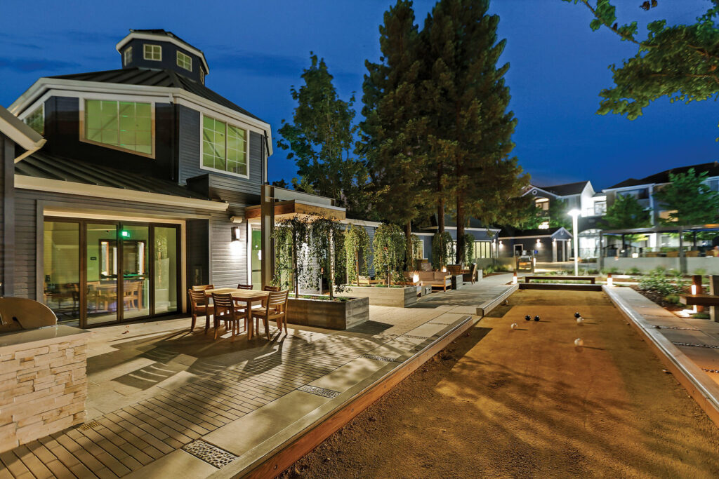 Exterior view of blue leasing center building with outdoor seating, grilling, fire pits and Bocce Ball court