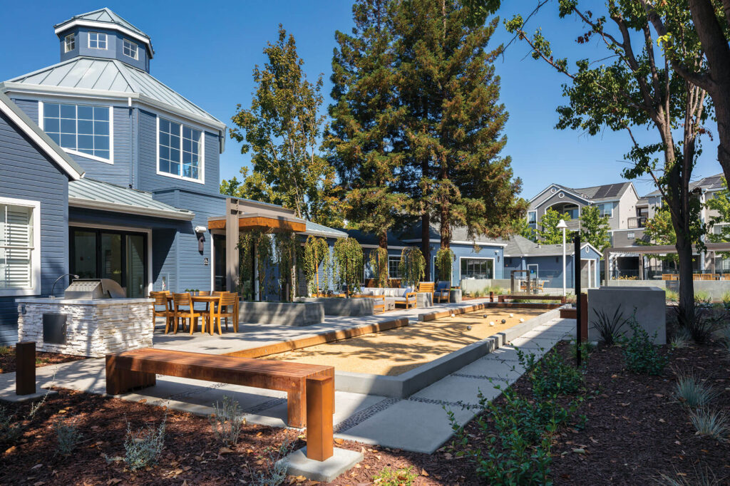 Exterior view of blue leasing center building with outdoor seating, grilling, fire pits and Bocce Ball court